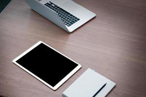 laptop aberto de estação de trabalho com tablet digital de tela em branco na mesa de madeira foto
