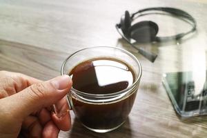 mão segurando a xícara de café ou chá e fone de ouvido voip, telefone inteligente na mesa de madeira, efeito de filtro foto