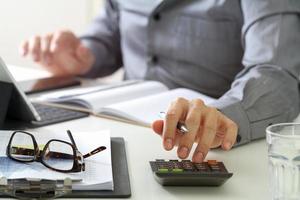 mão de empresário trabalhando com finanças sobre custo e calculadora e latop com celular na mesa no escritório moderno foto