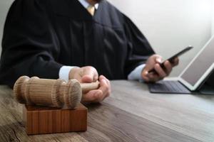 conceito de justiça e direito. juiz masculino em um tribunal com o martelo, trabalhando com telefone inteligente, teclado de encaixe de computador tablet digital na mesa de madeira foto