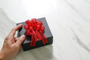 presentear, mão de homem segurando uma caixa de presente em um gesto de dar no fundo da mesa de mármore cinza branco foto