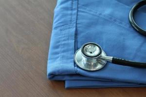 estetoscópio com casaco de médico azul na mesa de madeira com dof raso uniformemente combinado e fundo foto