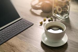 xícara de café e teclado inteligente dock de mesa digital, ervas de flores de vaso, fone de ouvido de música, óculos na mesa de madeira, efeito de filtro foto