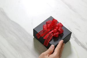 presentear, mão de homem segurando uma caixa de presente em um gesto de dar no fundo da mesa de mármore cinza branco foto