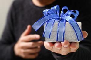 presentear, mão de homem segurando uma caixa de presente em um gesto de doação. fundo desfocado, efeito bokeh foto