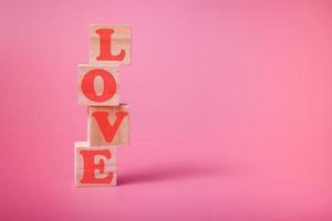 a palavra amor tem a forma de um coração em cubos de madeira em um fundo rosa. foto