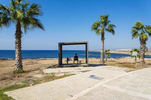 um homem sentado em um banco com vista para a ilha marítima de Chipre. foto