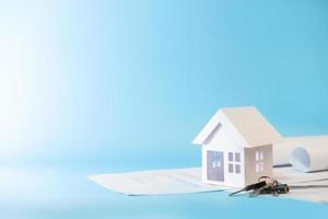 modelo de casa branca em documentos comerciais com chaves em fundo azul para plano de refinanciamento e conceito imobiliário. foto