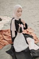 linda modelo feminina islâmica vestindo moda hijab, um vestido de noiva moderno para mulher muçulmana sentada na areia e na praia. retrato um modelo de menina asiática usando hijab se divertindo na praia com árvores foto