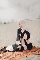 linda modelo feminina islâmica vestindo moda hijab, um vestido de noiva moderno para mulher muçulmana sentada na areia e na praia. retrato um modelo de menina asiática usando hijab se divertindo na praia com árvores foto