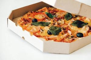 pizza em uma caixa de papelão em um fundo de mesa branca. copiar, espaço vazio para texto foto