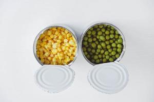 duas latas abertas com milho e ervilhas em um fundo branco. vista do topo. copiar, espaço vazio para texto foto