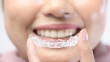 jovem mulher sorridente segurando aparelho invisalign sobre estúdio de fundo branco, saúde bucal e conceito ortodôntico. foto