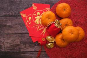 fundo de feen do ano novo chinês. conceito de festival de fu de personagem chinês. tangerinas, envelopes vermelhos, lingotes de ouro e bule de chá em pano vermelho com madeira velha que representa sorte foto