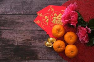 conceito de festival de ano novo chinês. tangerinas, envelopes vermelhos e lingotes de ouro em pano vermelho com fundo de madeira velho decorado com flor de ameixa. caractere chinês fu que significa sorte. foto