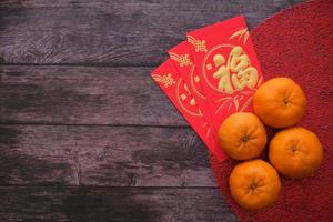 conceito de festival de ano novo chinês. tangerinas e envelopes vermelhos pano vermelho com fundo de madeira velho. caracteres chineses significam rico, rico, saudável e feliz. copie o espaço para o texto. foto