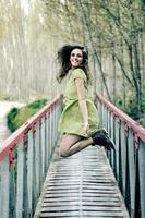 linda loira, vestida com um vestido bege, pulando em uma ponte rural foto