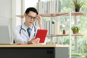 médico lendo o registro do paciente do tablet digital no escritório do hospital foto