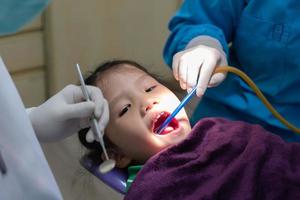 jovem dentista e assistente dental fazendo procedimento para tratar cárie dentária para menina na clínica foto