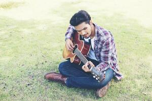 homem jovem hippie praticou guitarra no parque, feliz e gosta de tocar guitarra. foto