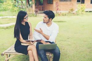 jovem casal de educação sentado no banco fala sobre estudar ao ar livre e bom tempo. foto