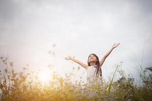 menina asiática bonitinha de pé entre o dia de sol do campo de flores roxas. liberdade desfrutando com a natureza. foto