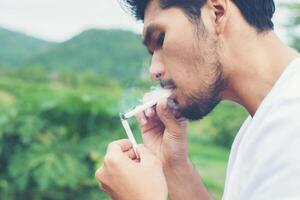homem jovem hippie descansando, fumando cigarro com natureza e brisa fresca. foto
