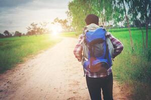 feche o homem jovem hippie com mochila no ombro andando pela zona rural. foto