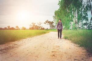 homem jovem hippie com mochila no ombro andando pela zona rural. foto