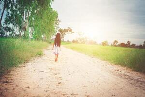 menina com vestido de cabelo comprido está se afastando de você na estrada rural. foto