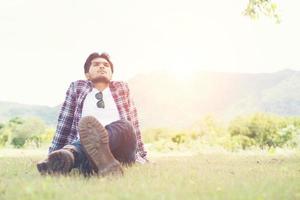 homem jovem hippie sentado na grama do parque, divirta-se com ar de brisa natural e fresca. foto
