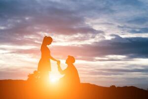 silhueta de homem pede mulher em casamento no fundo da montanha. foto