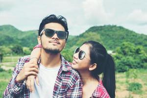 Feche o retrato de casal feliz hipster apaixonado usando óculos abraços e se divertindo com fundo de montanha de natureza. foto