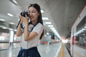 uma jovem e bela turista asiática, fotógrafo tirando fotos instantâneas com câmera de filme, sorriso e prazer na plataforma da estação de trem, estilo de vida de viagem feliz por viagem de férias de transporte de metrô.