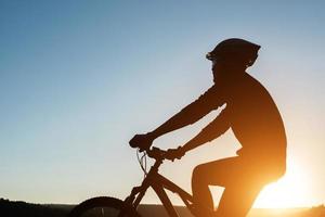 silhueta de um homem em mountain bike durante o pôr do sol.