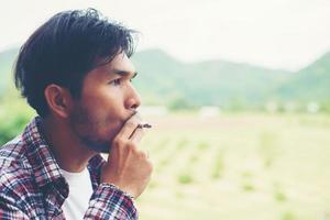 homem hipster fumando cigarro, atrás de uma montanha. entre o ar fresco da manhã. foto