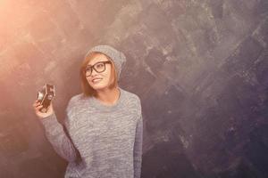 mulher hipster sorridente usando óculos segurando uma câmera retro contra fundo bege foto