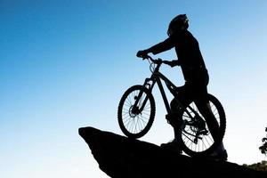 silhueta do atleta em pé na rocha com bicicleta foto