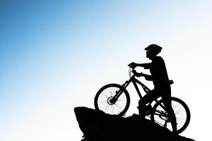 silhueta do atleta em pé na rocha com bicicleta foto