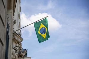 bandeira do brasil. bandeira brasileira exibida em um poste na frente da casa. bandeira nacional do brasil acenando em uma casa pendurada em um poste na porta da frente de um prédio. foto