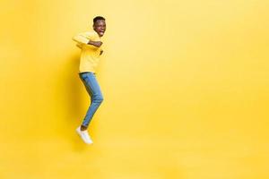 jovem africano animado alegre pulando com as mãos apertando no fundo do estúdio amarelo isolado com espaço de cópia foto