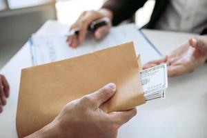 empresário secretamente dando um suborno, dando notas de dinheiro no documento de contrato de envelope. foto