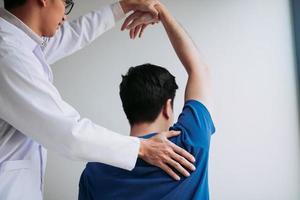 quiroprático esticando um braço de jovem no consultório médico foto