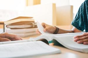 estudantes em uniformes universitários sentados à mesa na biblioteca da escola e lendo um livro juntos. foto