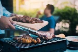 close-up homem de mão asiática está beliscando a carne de porco na grelha e segurando-a para amigos que estão comemorando na parte de trás. foto