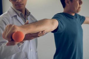 fisioterapeuta asiático ajudando um paciente levantando halteres a trabalhar em sua recuperação com pesos na sala da clínica. foto