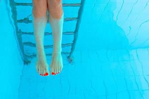 Pernas de mulher europeia caucasiana branca adulta com pedicure ultravioleta laranja debaixo d'água na piscina. verão. pernas subaquáticas engraçadas na piscina, férias e conceito de esporte. foto