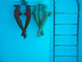as pernas do homem afro-americano adulto e as pernas da mulher caucasiana debaixo d'água na piscina. conceito de esporte, recreação, férias e amizade foto