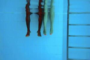as pernas do homem afro-americano adulto e as pernas da mulher caucasiana debaixo d'água na piscina. conceito de esporte, recreação, férias e amizade foto