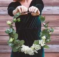 mãos femininas segurando uma coroa decorada de flores e folhas em um fundo de madeira foto